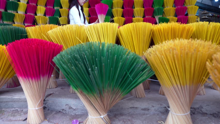 A young Vietnamese woman in a white national costume arranges colorful incense sticks in Hue, Vietnam.