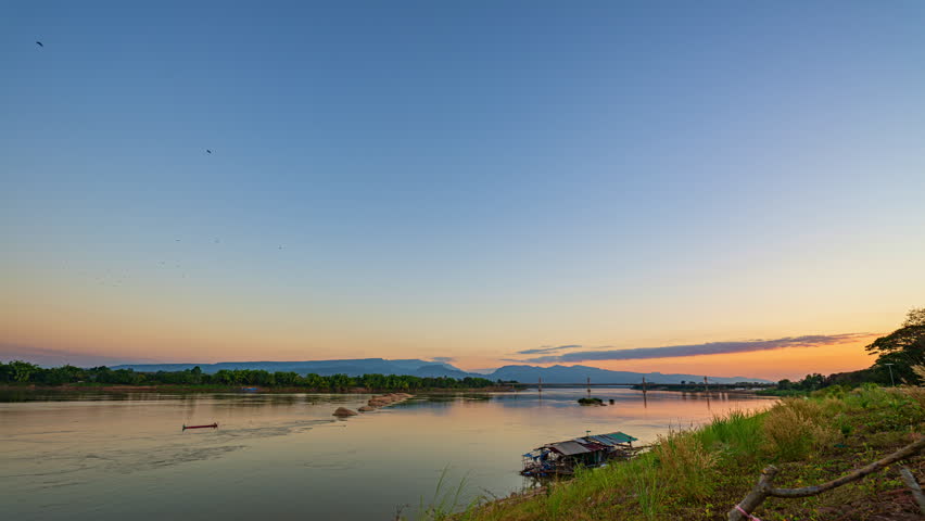 Time lapse A dreamlike sunset casting golden light over the Mekong River and the Fifth Thai–Lao Friendship Bridge in Bueng Kan, creating a surreal and peaceful atmosphere. colorful Reflection