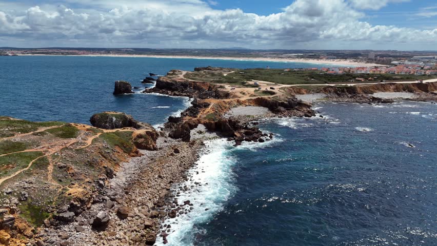 Aerial View of Rugged Coastal Peninsula With Natural Rock Bridge and Distant Sandy Beach Under Cloudy Sky
