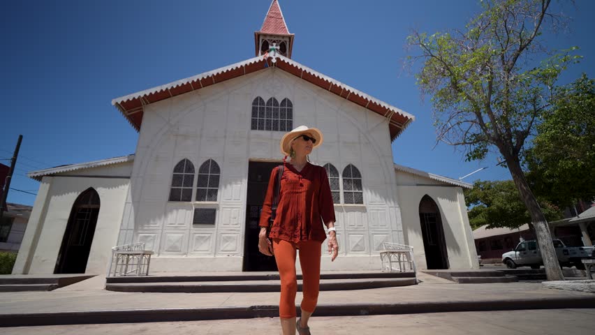 Mature woman walks around Santa Barbara church in Santa Rosalia, observing the architecture and enjoying the sunny day in Baja California, Mexico.