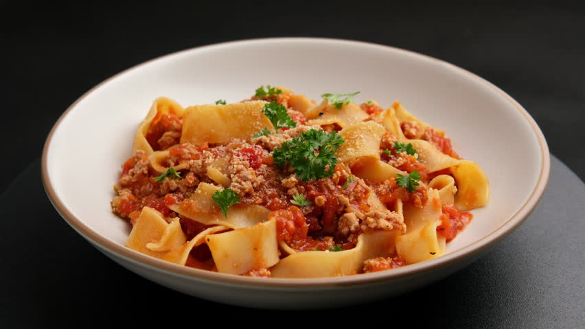 pappardelle pasta with Ground meat and tomato,spaghetti with a meat based bolognese tomatoes,served on white plate with parmesan cheese.