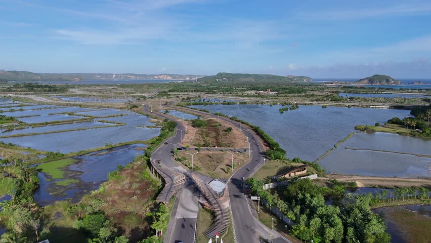 Aerial Drone View of Rural Coastal Landscape with Roads, Wetlands, and Aquaculture Ponds under Blue Sky