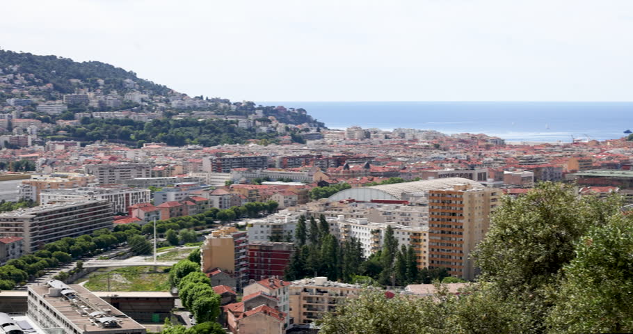 Panoramic Nice city view with residential buildings and Mediterranean sea horizon in background. Urban French Riviera scenery from Cimiez hill with traditional red rooftops and modern apartment blocks