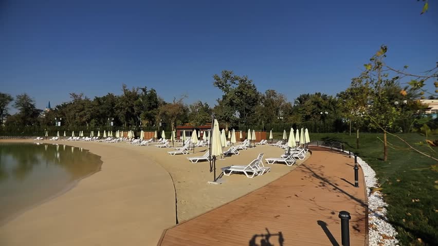 Walk along the shore of the city lake with a sunbathing beach and sun loungers. Sunny summer day. Slow Motion