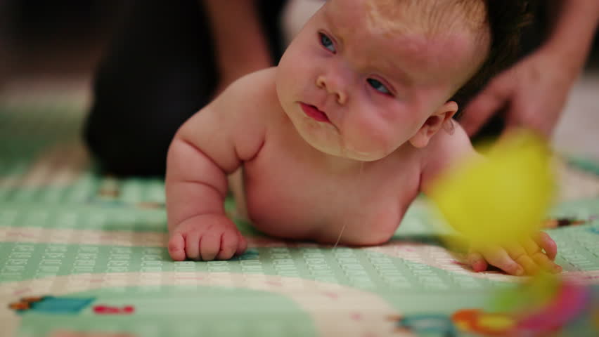 A small baby lying on their tummy and back on a padded surface