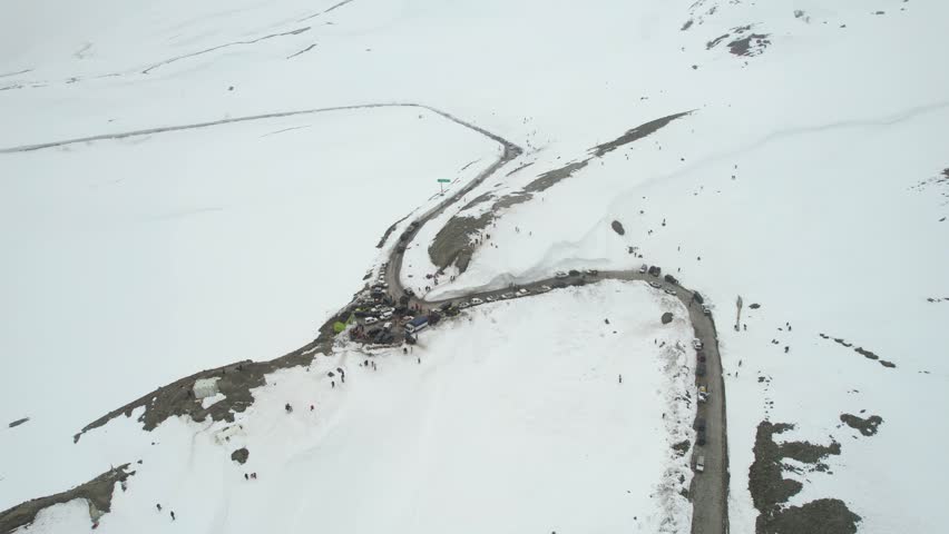 Aerial drone orbit wide view of tourists exploring snowy mountains near Shinkula Top Pass and Sissu in Himachal Pradesh with parked 4X4 vehicles winding roads in Ladakh Himachal Pradesh India during w