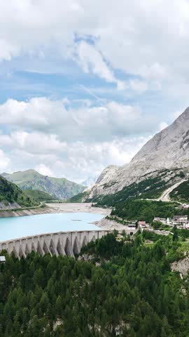 Turquoise lake behind large concrete dam in mountainous landscape with green forest.