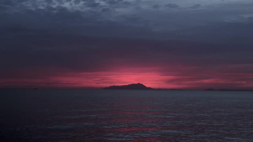 Calm ocean water at dramatic sunset with dark clouds and colorful evening sky over the sea.