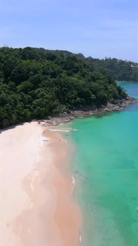 Aerial drone view of tropical beach with turquoise water, white sand, and lush jungle coastline in Phuket, Thailand on sunny day.