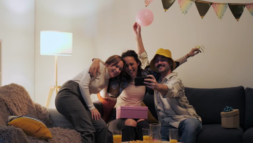 Happy group of friends taking selfies with a smartphone while celebrating a birthday at home