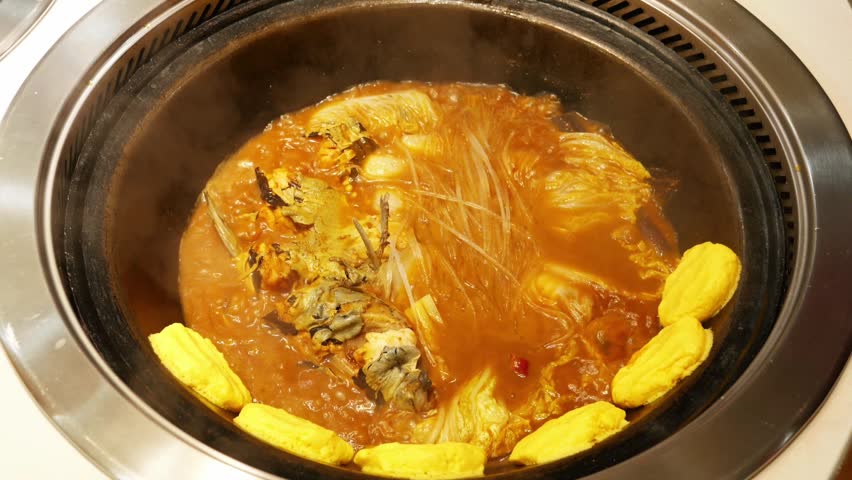 A cooked Chinese stew of fish and noodles in a cast iron wok with golden corn cakes steaming.