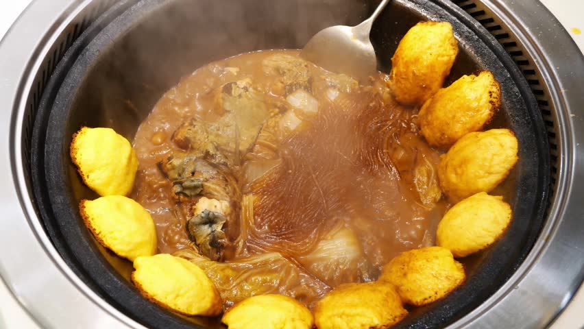 A cooked Chinese stew of fish and noodles in a cast iron wok with golden corn cakes steaming.