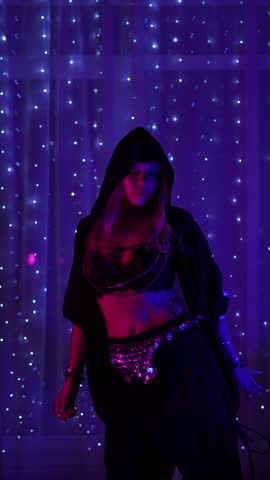 Young woman performing belly dance with hip shimmies and figure-eight movements in purple neon light. Mystical oriental dance performance with smooth body motion and feminine energy