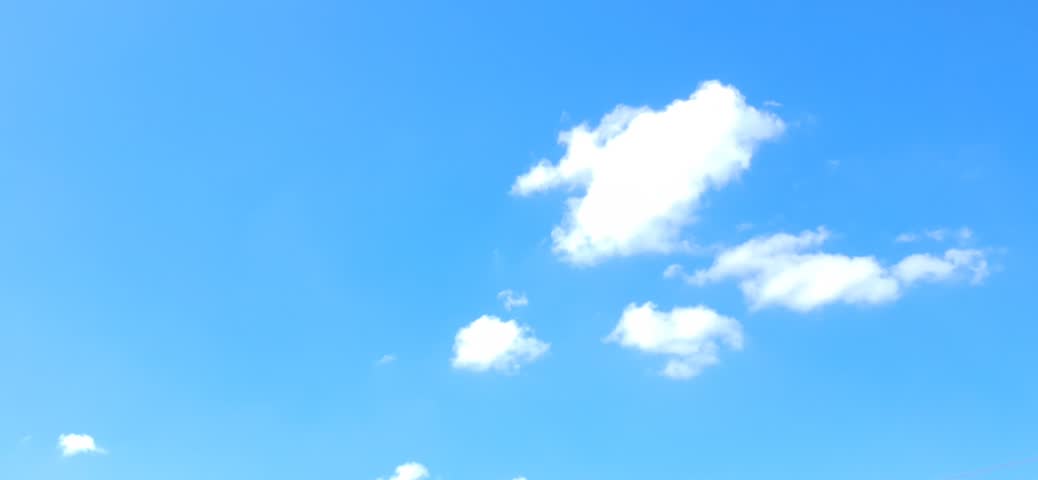 Sunny day landscape with soft white cumulus clouds drifting across a bright blue sky.