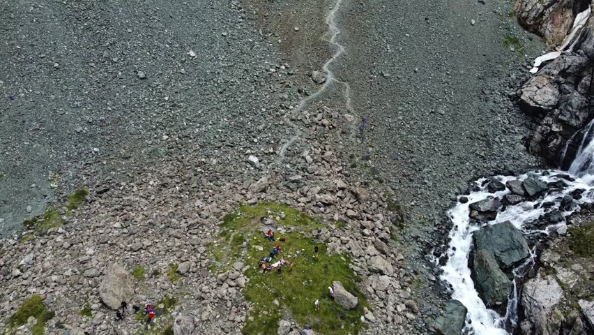 Top down view of hikers resting on green grass near winding rocky trail and mountain stream, adventure concept, Ala-Kul, Kyrgyzstan