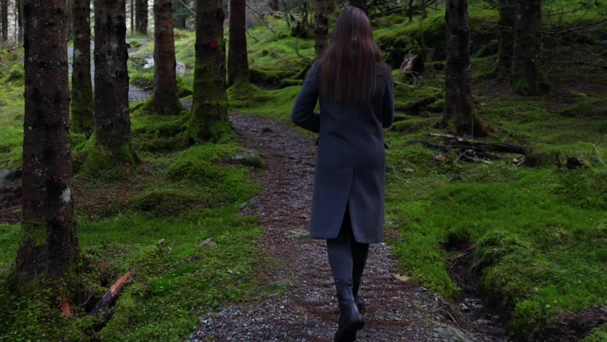 Woman Hiking Uphill Along Moss Covered Forest Trail