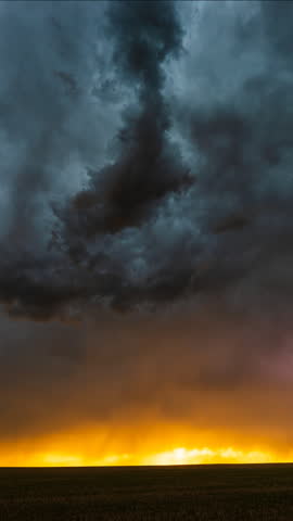Lightning streaks across dark storm clouds as warm orange sunset tones glow along the horizon, creating dramatic contrast, intense atmosphere, vibrant sky colours and a cinematic severe weather scene