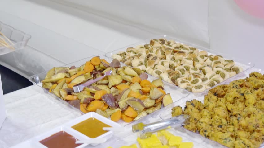 Vibrant appetizer buffet featuring roasted sweet potatoes, savory pastries, vegetables, and traditional yellow sweets served with assorted dipping sauces. 
