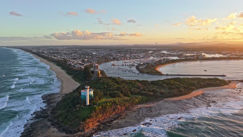 Drone aerial panorama of the Mooloolah River mouth and Point Cartwright at sunrise, Sunshine Coast Queensland. Ocean beach, marina channel, anchored boats and glowing coastal skyline under warm morning light.