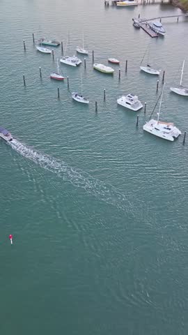 Drone aerial view of moored yachts and catamarans on the Mooloolah River beside sandy beach and coastal parkland, Sunshine Coast Queensland. A small boat cruises through calm turquoise water at sunset.