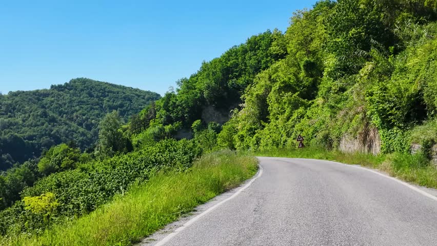 Camera moves forward on a winding rural road under a clear blue summer sky