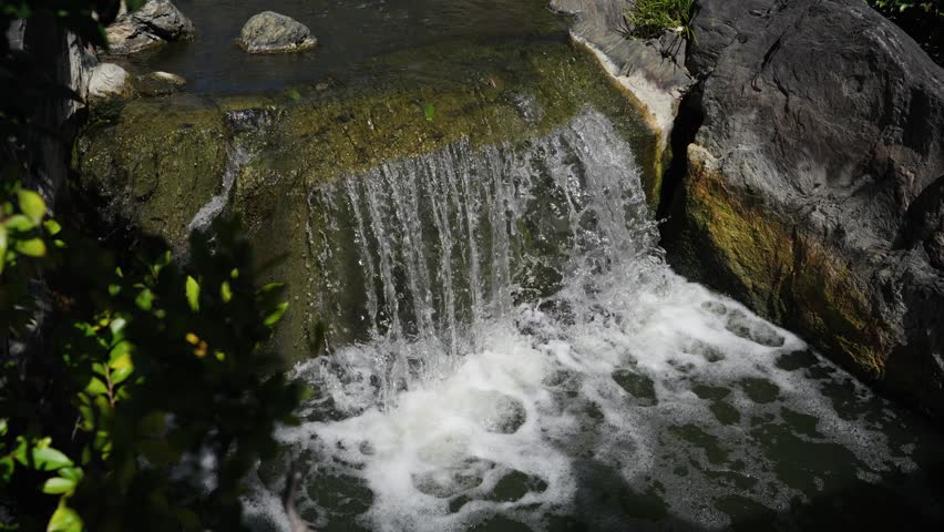 Water cascading over mossy algae covered rock into foaming pool in Japanese shrine garden Tokyo Japan