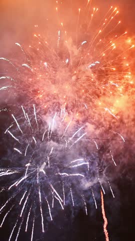 colorful fireworks display during holiday celebration with glowing explosions and illuminated smoky sky.