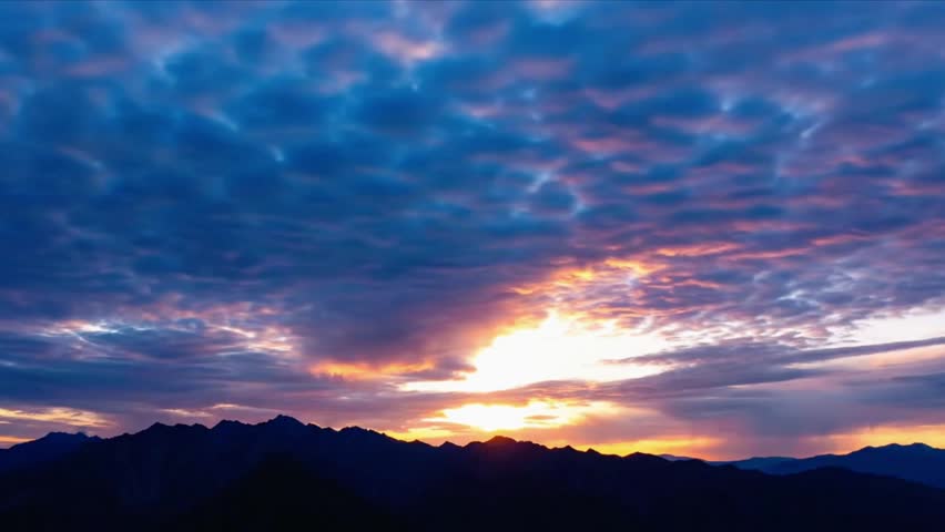 Sunset light illuminates dramatic clouds over mountain peaks. Nature