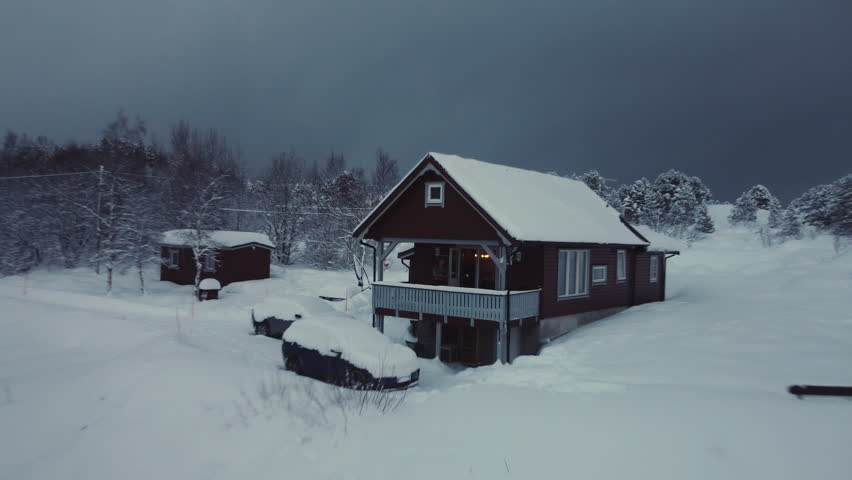 Drone shot of a solitary wooden cabin buried in deep snow within a dense forest in the Lofoten Islands, Norway. Quiet winter solitude and remote living in the arctic wilderness