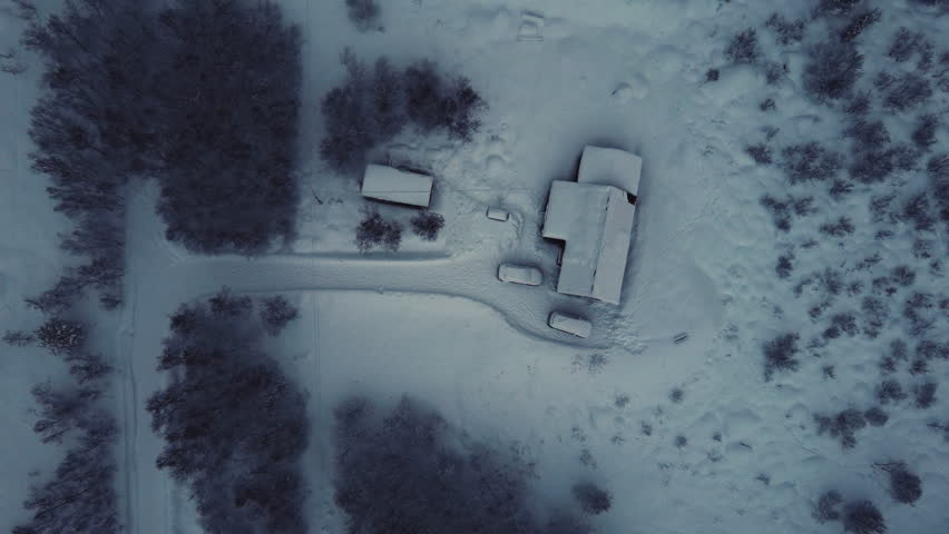 Aerial view of a lonely house and cars buried in deep snow within a dense arctic forest. Winter solitude and remote living in the wilderness of Lofoten Islands, Norway