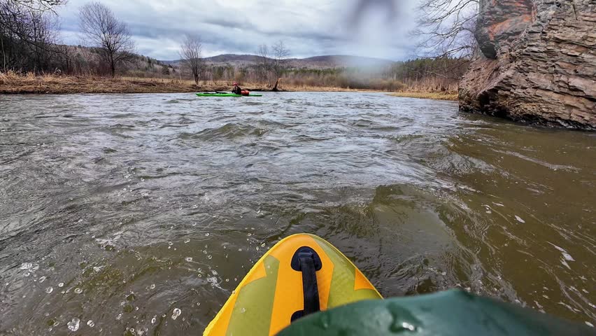 White paddler battling swift rapids redhatted kayaker leans into churning current, spray and waves surround, forested bank, highadrenaline protective gear visible, teamwork with nearby