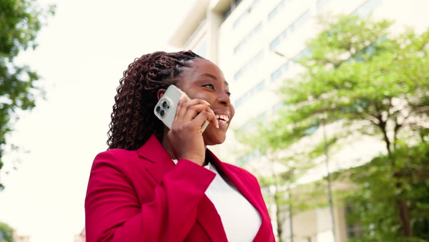 African corporate businesswoman enjoying a phone call while standing against a modern building