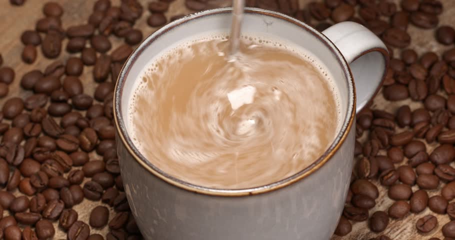 Hot instant coffee mix 3 in 1 being stirred in a cup close-up footage on a background of coffee beans.