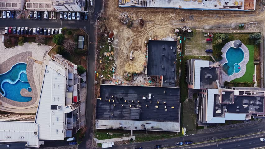 View shows construction work next to swimming pools in Nesebar, Bulgaria. Surrounding buildings are visible. The site is busy with workers and equipment in the area.
