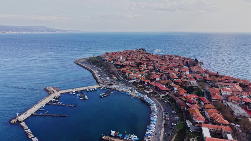 Nesebar in Bulgaria shows houses along the coast. Boats are docked in the harbor. The sea is nearby. The sky is clear. This view captures the layout of the town and water.