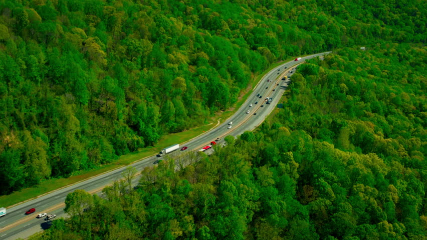 Red flatbed semi-truck moving along a curving two-lane highway surrounded by dense spring forest in the Appalachian
foothills of North Carolina.