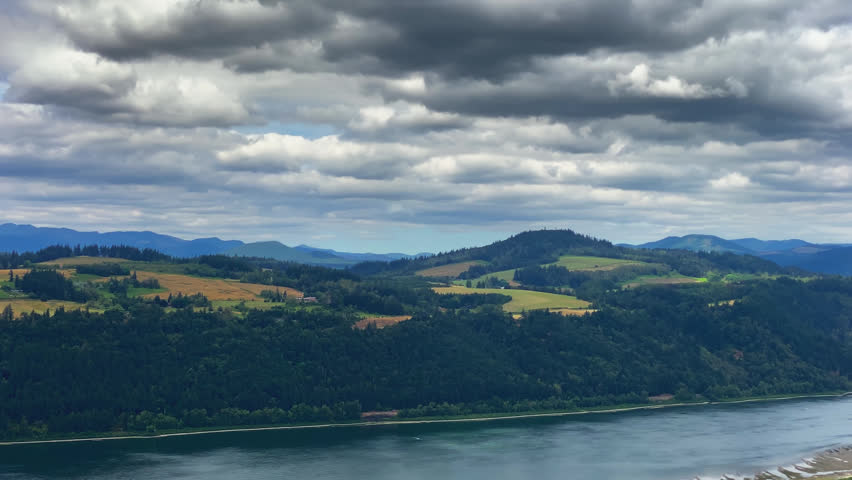 Panoramic view overlooking the Columbia River Gorge with winding river, forest covered hills and layered mountains under cloudy skies, aerial overlook