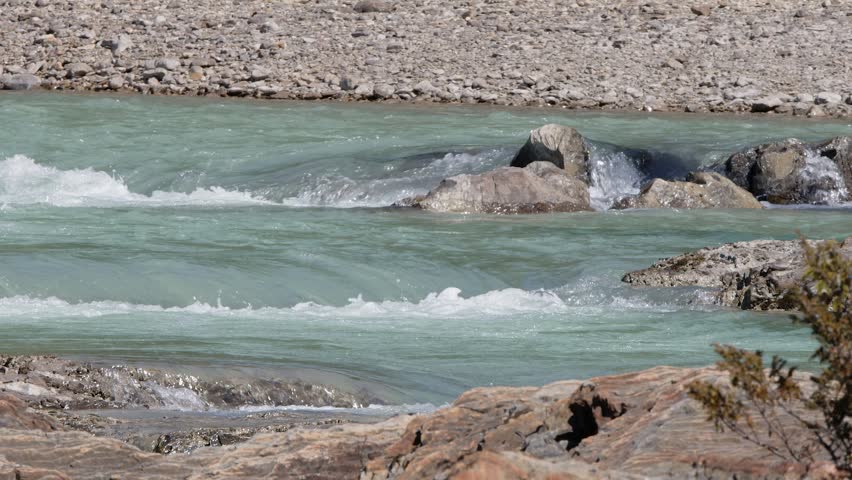 Turquoise glacial mountain river flows over bedrock riverbed outcrops