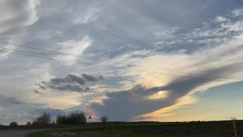 Dramatic pre-storm sky over a rural road at twilight. Heavy cumulus clouds and soft sunset light over a spring field landscape.