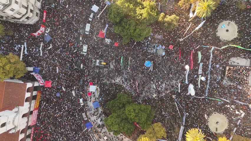 Huge crowd of people with banners and flags at university protest in Plaza de Mayo, Buenos Aires, Argentina. Aerial top-down ascending