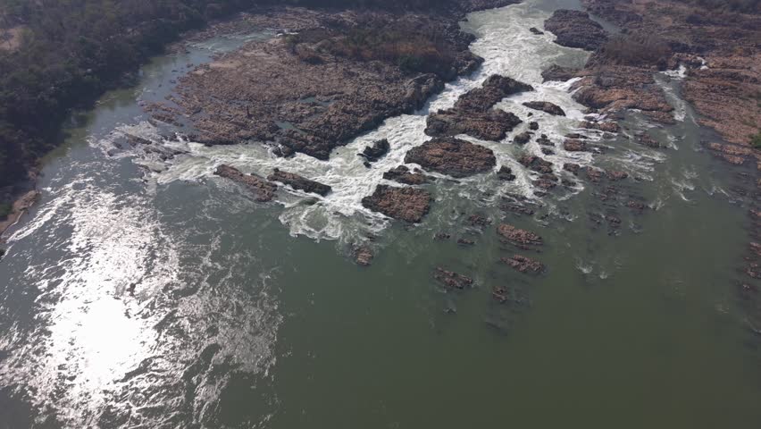 Aerial shot starting at high elevation, then descending over the falls and looking downstream from just above the water.