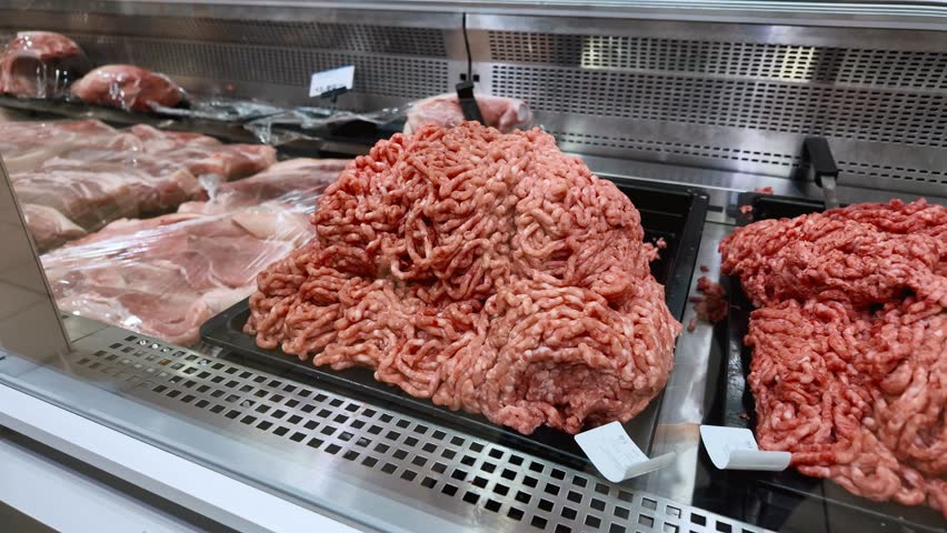 Raw minced meat on a tray inside a refrigerated display case in a grocery store's butcher section, ready for customers to purchase for cooking various meals like burgers or bolognese