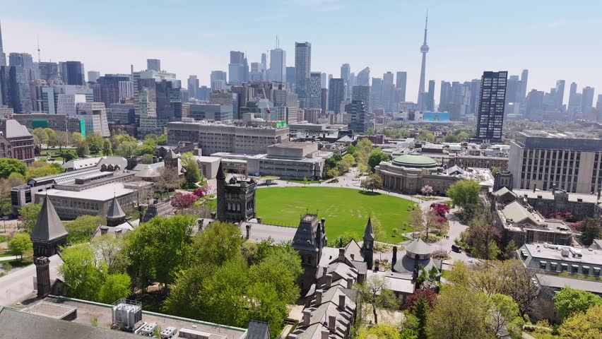 Aerial view flying forward over University College and tilting down to frame the large, vibrant green lawn of King