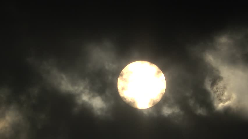 Dramatic view of the glowing sun completely surrounded by dense dark moving clouds, creating an intense high-contrast background during late afternoon.

