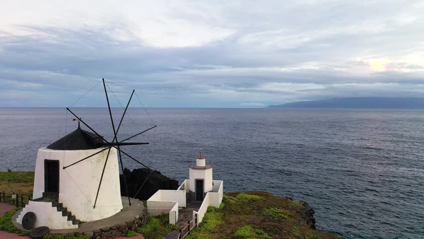 View of windmill near ocean with fields and clouds at sunset on a quiet evening in the countryside