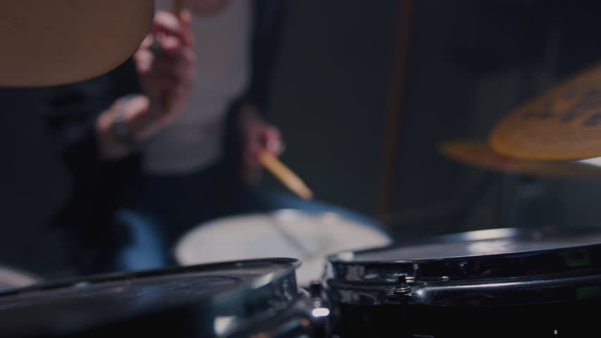 Young female drummer passionately playing a drum kit in a professional rehearsal studio, energetically striking cymbals and drums with drumsticks. Hair flying. Rock Feminist style. Woman power.