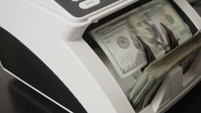 Money counting machine processing dollar bills in motion. Banking operation and finance concept with money movement. Counting money in motion. Counting dollar notes in a banking machine.