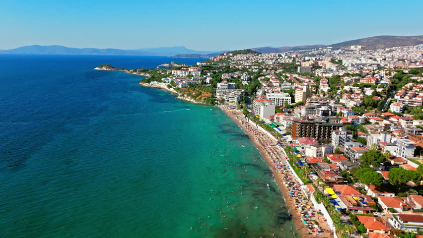 Aerial view of Ladies Beach in Kusadasi, Turkey. People swim and relax along the long sandy coast beside city buildings and blue Aegean water.