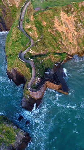 An aerial shot at Dunquin Pier in County Kerry, Ireland, starting near a top-down view of the pier before lowering and orbiting to reveal green cliffs, rugged coastline and changing sunset light.
