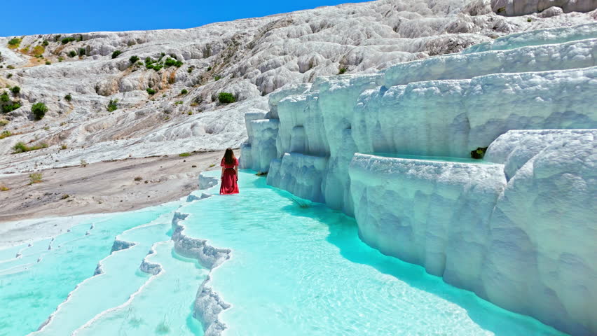 Woman traveler at Travertines of Pamukkale, Turkey. Female visitor walks through turquoise thermal pools beside tall white limestone terraces.